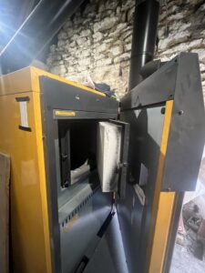 Yellow biomass boiler with door open, in a stone outhouse.