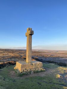 Stone Cross on hill side with moorland in background