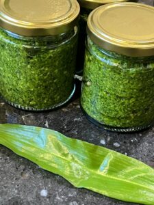 Two jars of garlic pesto next to a wild garlic leaf