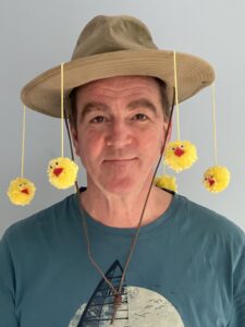 Man in Hat with yellow pom pom chicks suspended from it.