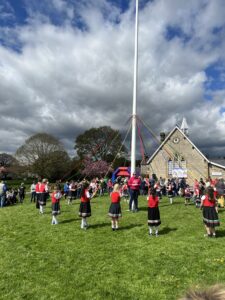 Children in red tops standing around a village maypole