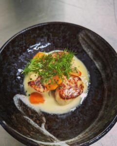 Scallop dish on a black plate with sauce and garnish