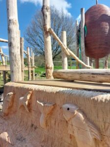 Adventure playground with wooden carvings next to rope walk.