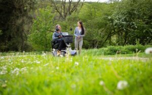 Man and woman walking on a path through a field. Man is on a mobility scooter