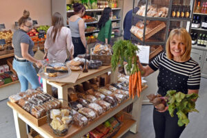 Woman in stripy top holding up some veegetables in a farm shop.