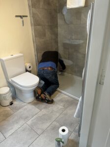 Man on knees filling the shower trap in an ensuite bathroom