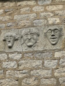 3 satirical male faces carved into stone on house