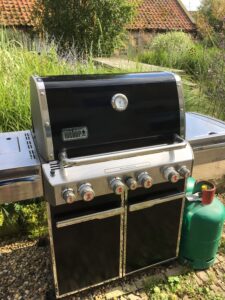 Larege black Weber BBQ in garden with green gas bottle