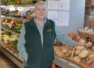 Woman in green gilet in fruit and veg shop smiling 