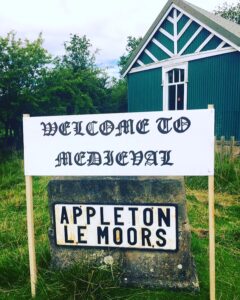 Sign saying "Welcome to Medieval Appleton Le Moors" next to green and white Reading Room.