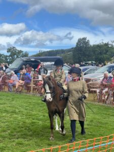 Small child on pony being led round show ring by woman