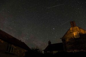 farm house with starry night behind it, showing shooting stars