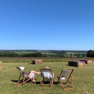 Couple sitting in two deck chairs, overlooking the North York Moors. with hay bales in background. 