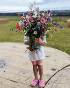 Small child holding a huge bouquet of wild flowers in front of her face.