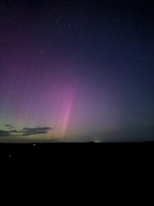 NOrthern lights over North York Moors; white column with pink and purple lights in night sky.