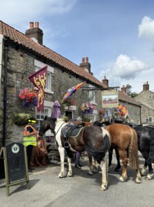 3 horses outside village pub the Moors. Handing baskets and flags decorating the building.