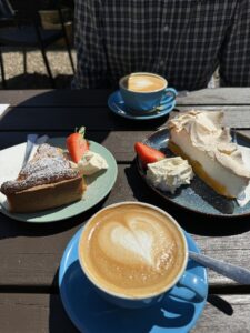 Two cups of coffee with hearts on the top along with two plates of cake