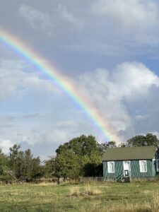 Green and white one storey building with rainbow behind in blue sky