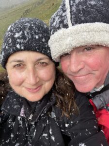 Man and woman wearing hats, smiling at camera and covered in snow