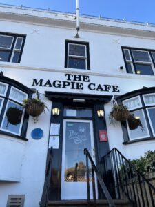 Black and white building with steps leading to front door. Sig reads The Magpie Cafe