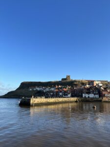 Whitby Abbey on hill side overlooking the sea and a pier. View from the pier