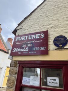 A whilte building with a sign above the door in maroon, saying "Fortunes Cured Kippers Est 1872"