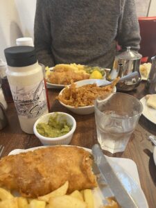 A meal of fish and chips on a table with tea and peas