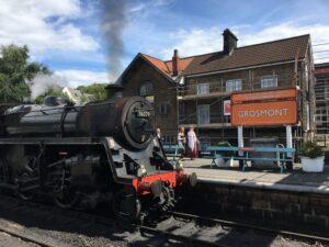 Steam train arriving at Grosmount Station with green benches on platform