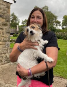 Woman in black top and pink trousers holding a Jack Russell dog.