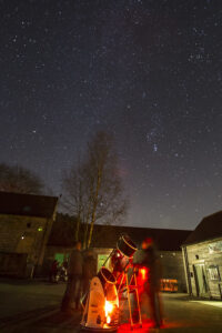 People looking through telescope at night sky in a court yard