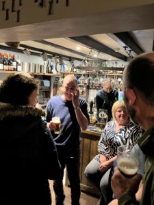 Man drinking a beer at bar in pub, filled with happy locals.