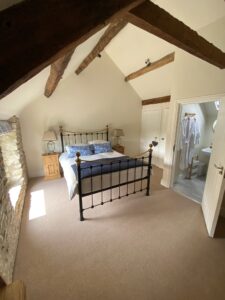 Iron double bedroom with beams and white walls. Door open into an ensuite