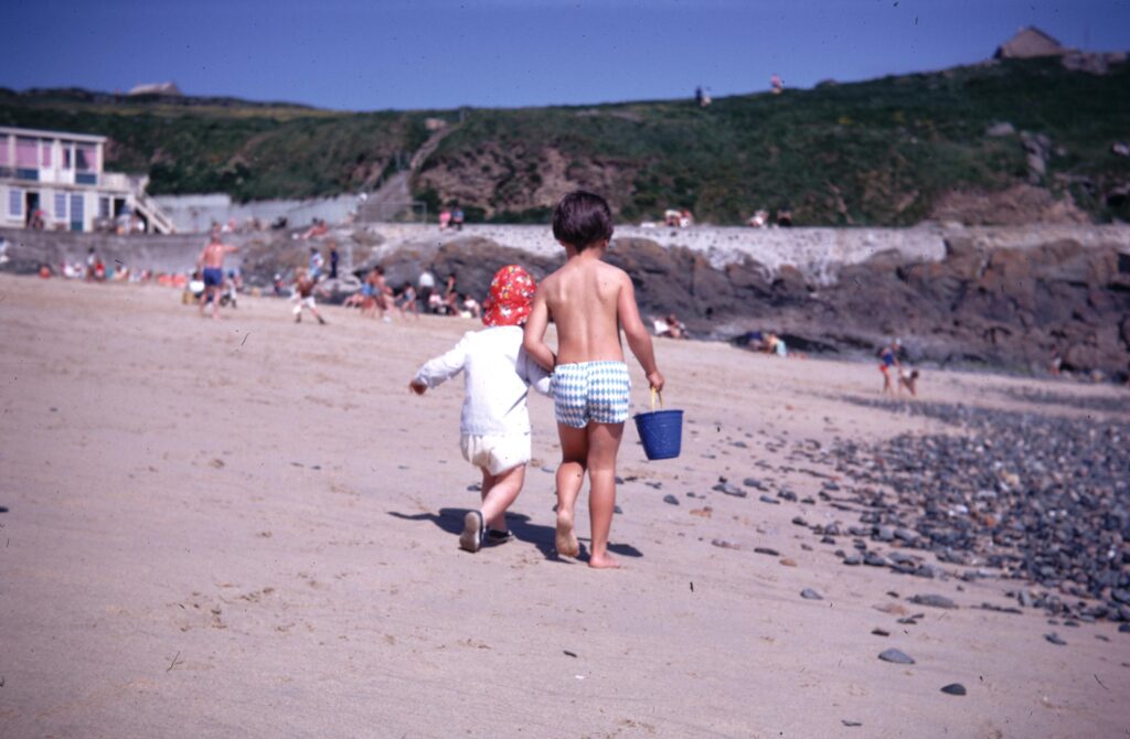 Two small children on a sandy beach walking away from the camera.