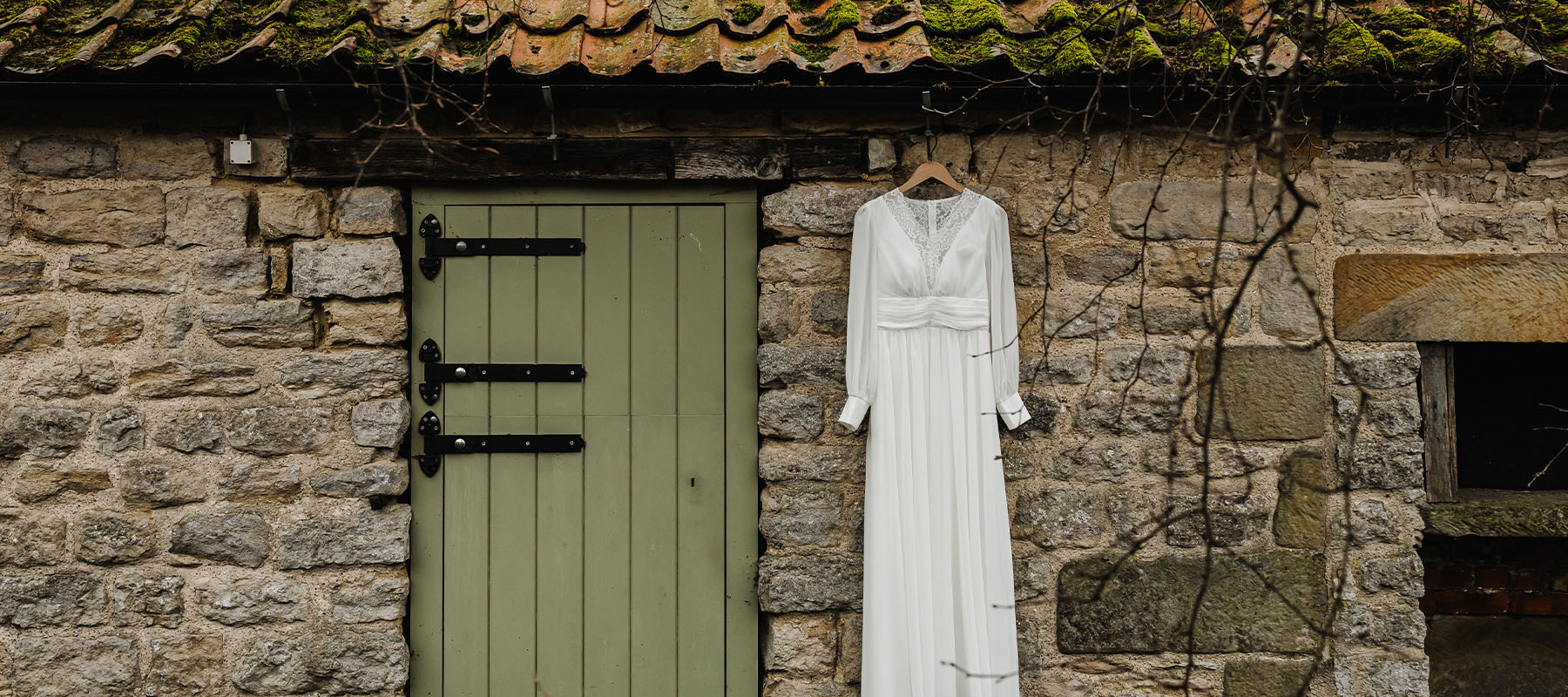 Wedding dress hanging on a green barn door against the stone wall at the Long Barn in North York Moors