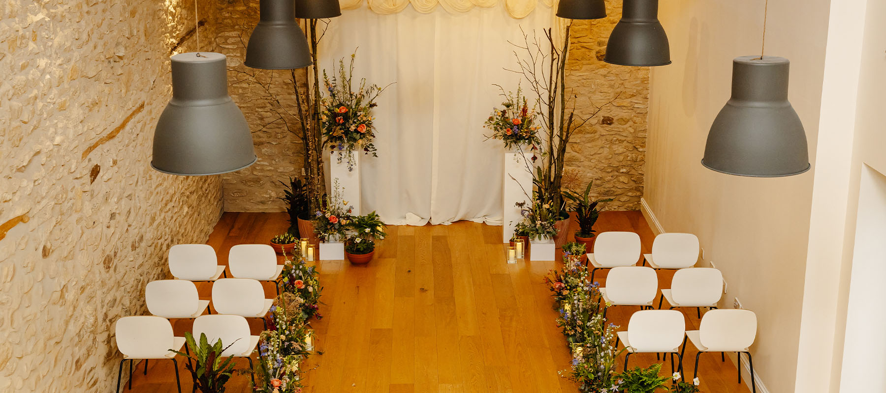 Intimate wedding ceremony setup in the Long Barn, North York Moors with white chairs, floral arrangements and stone walls