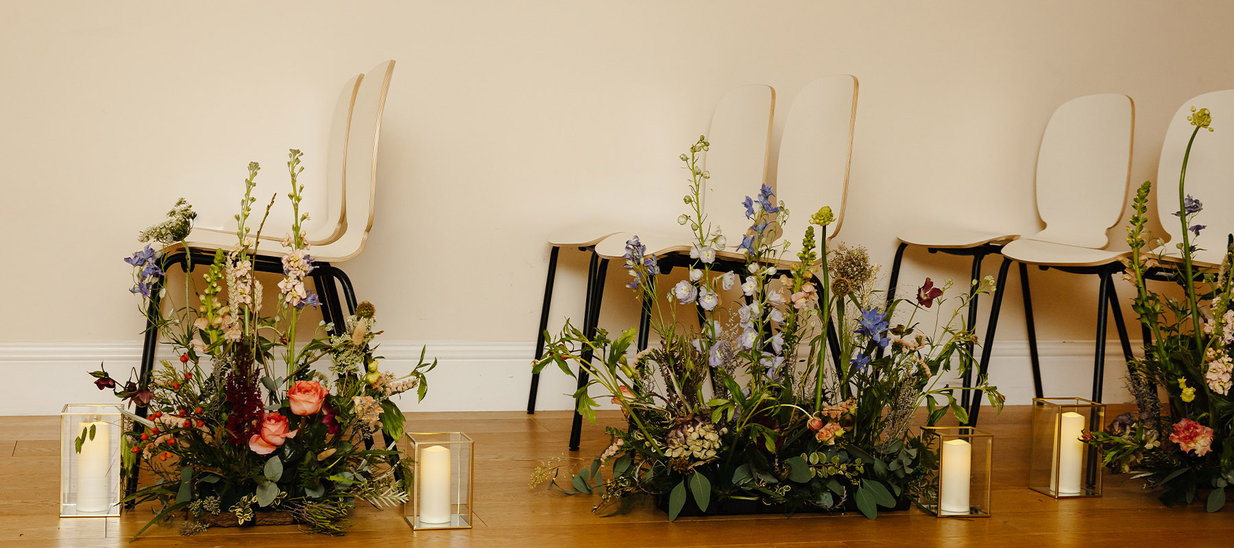 Close-up of wedding ceremony chairs lined with seasonal flowers and candle lanterns in the Long Barn, North York Moors.