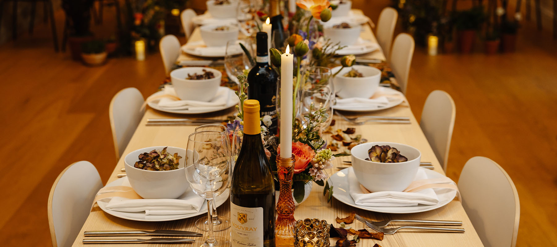 Long banquet-style wedding table set for an intimate celebration with flowers, candles and wine